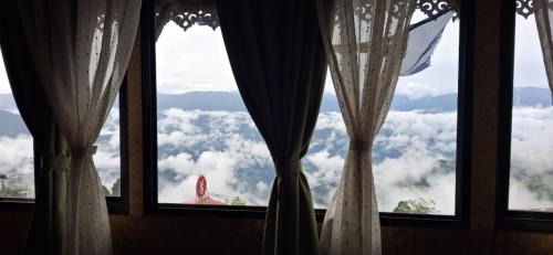 a window with curtains and a view of clouds at Monratino Himadrie -2 mins walk from Mall Road - All rooms have Kanchenjunga Mountain View in Darjeeling