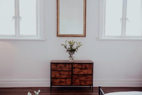 a vase of flowers on a dresser in a room with two windows at Holmfirth converted bank- centre of Town - Austen- Archive in Huddersfield
