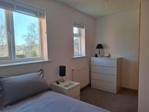 a bedroom with a bed and a dresser and two windows at Cosy Manorfield Holiday Home in Kent