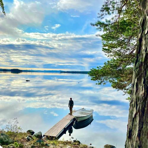 a man standing on a dock with a boat on a lake at Haven Islands Treehouse on a private island in Torrflonäs
