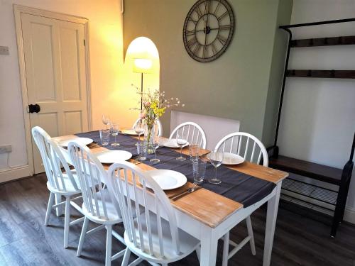 a dining room table with white chairs and a clock on the wall at Modern Bright 3 Bedroom House in Lincolnshire