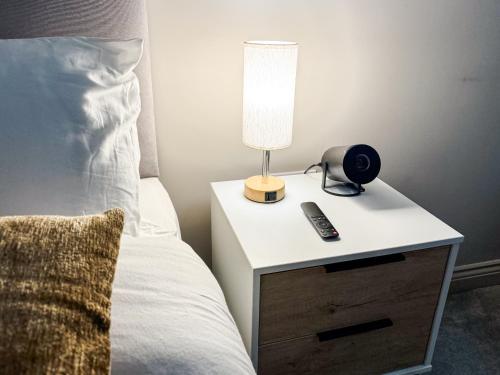 a bedside table with a lamp and a remote control on it at Prime Leeds- Spacious Cinema apartment in Central Station