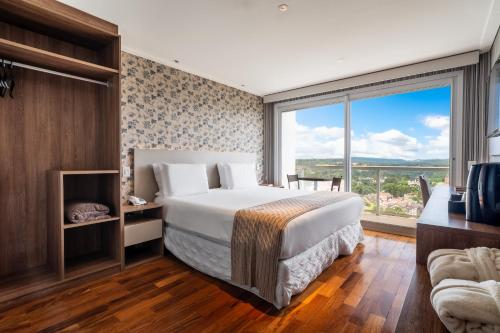 a bedroom with a large bed and a large window at Chris Wellness Resort Hotel in Campos do Jordão