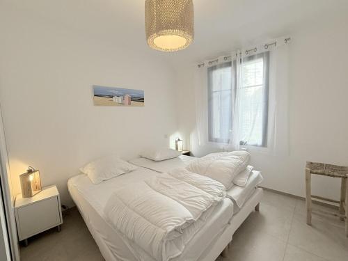Una cama blanca en una habitación blanca con una ventana. en La petite grole, en Saint-Pierre-dʼOléron