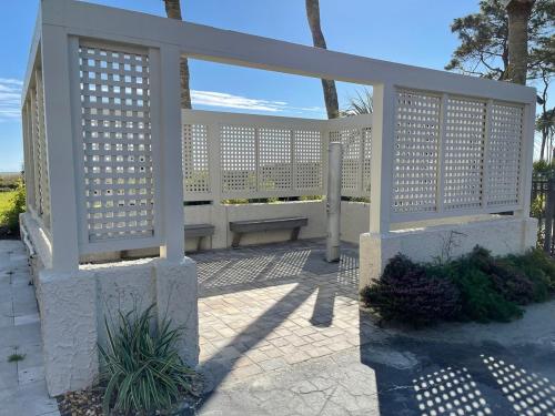 a white pergola with a bench on a patio at Coastal Getaway Oceanview Condo in Hilton Head in Hilton Head Island