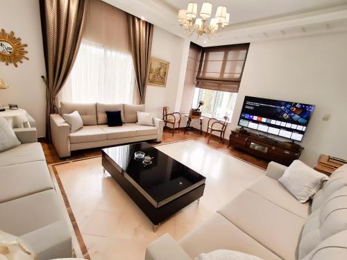 a living room with white furniture and a flat screen tv at L'Orchidée - Suites de Luxe avec Piscine Chauffée et Vue sur le Lac de Tunis in Tunis
