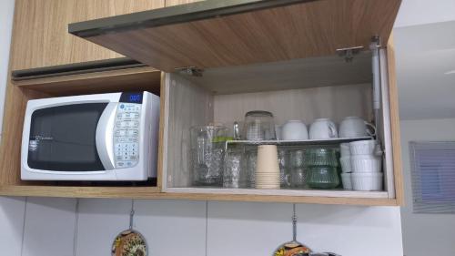 a microwave and some cups and glasses in a kitchen at Apartamento com Suíte em Bertioga Indaiá 150 metros da Praia in Bertioga