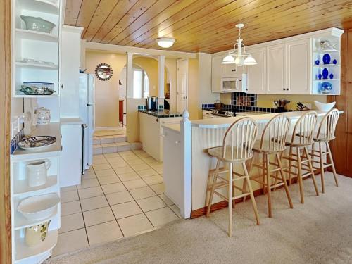 a kitchen with white cabinets and a bar with stools at A Charm of Finches in Surf City