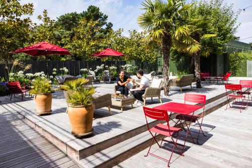 a group of people sitting on a patio with red chairs and tables at Hotel De Diane in Sables-dʼOr-les-Pins