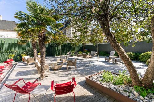a patio with chairs and tables and palm trees at Hotel De Diane in Sables-dʼOr-les-Pins