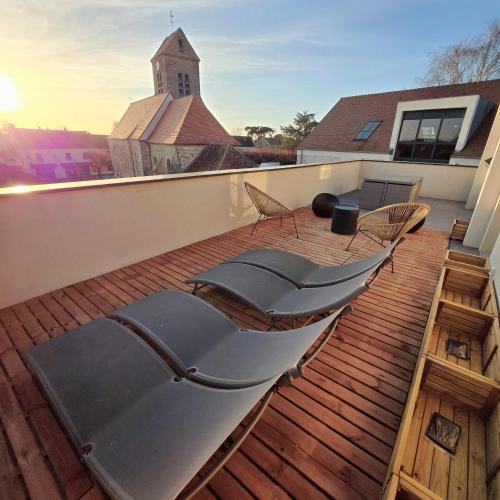 a deck with chairs and a church in the background at Le Break Douceur in Réau