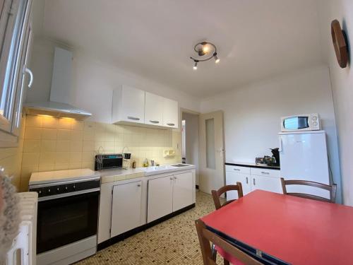 une petite cuisine avec des placards blancs et une table rouge dans l'établissement Very nice T3 near downtown Tarbes Marcadieu, à Tarbes