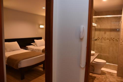 a room with two beds and a bathroom with a shower at Hotel San Marcos in Paipa