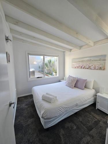 a white bedroom with a large bed with a window at Cygnets in Lake Munmorah