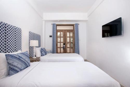 two beds in a white room with a tv at Adhisthana Hotel Yogyakarta in Yogyakarta