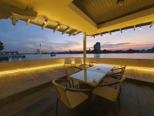 a table and chairs on a deck with a view of the water at Chao phraya riverfront house Baan Rimphraya in Bangkok