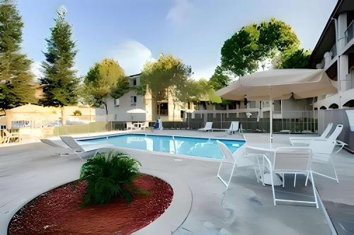 a swimming pool with chairs and a table and an umbrella at Inn at Rohnert Park in Rohnert Park