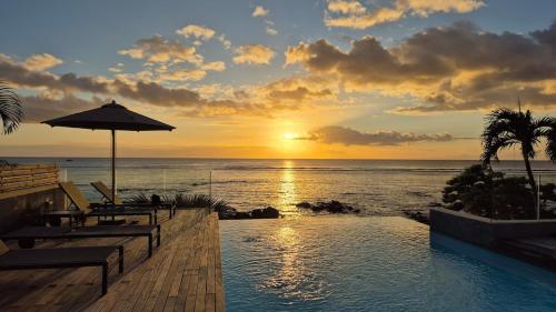 a swimming pool with a sunset over the ocean at Beachfront Chic Penthouse in Rivière Noire
