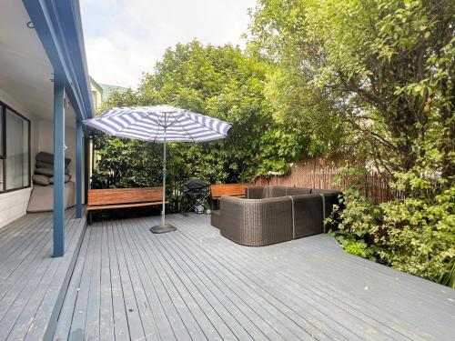 a patio with an umbrella and a couch and a bench at 6 Beds 2 Bathrooms Private Holiday Home in Akaroa