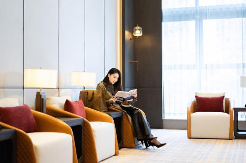 a woman sitting in a chair reading a book at Pullman Renhuai Chuangmeng in Zunyi