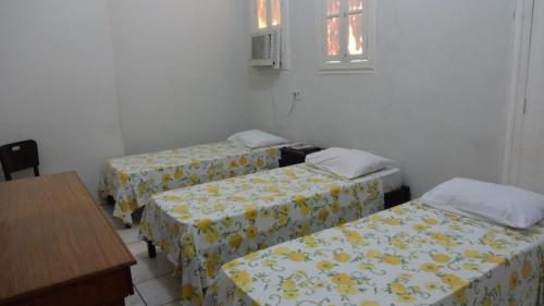 a room with three beds with yellow and white sheets at Hotel Central in Recife