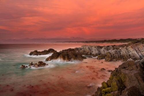 a sunset over the ocean with rocks in the water at Cliff Lodge in Gansbaai