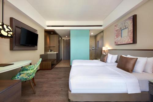 a hotel room with two beds and a desk and a television at Mercure Bali Legian in Legian