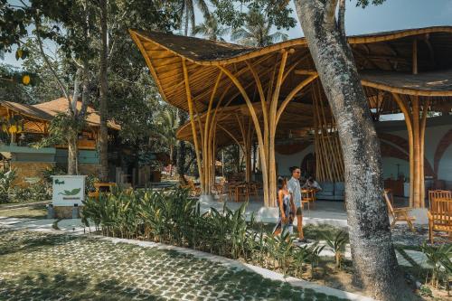 a man walking past a resort with a wooden pavilion at Tropik Resort Lombok in Selong Belanak