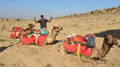 a man standing next to four camels in the desert at Desert Vista Camp Jaisalmer in Jaisalmer