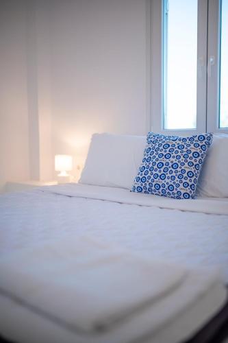a white bed with a blue pillow and a window at Sunrise Villa Santorini in Vourvoulos