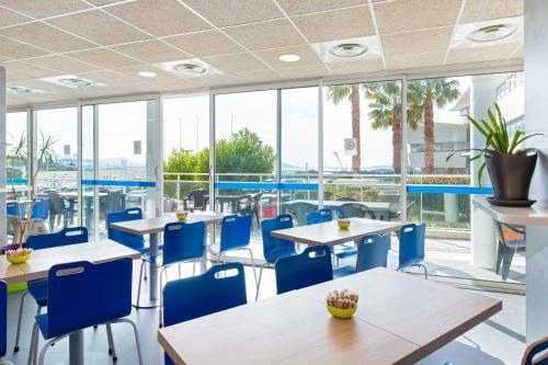 une cafétéria avec des tables, des chaises bleues et des fenêtres dans l'établissement ibis budget Marseille L'Estaque, à Marseille