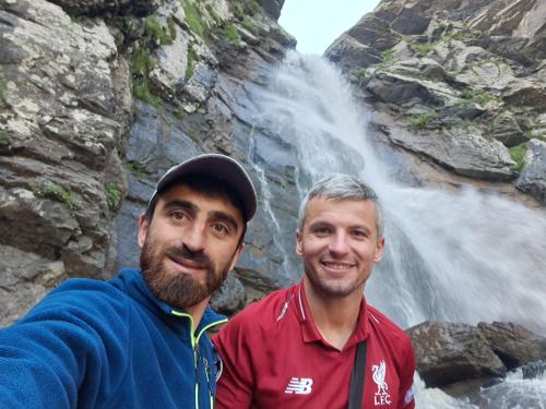 two men standing in front of a waterfall at Xinaliq Khinalig İzzet's Riverside Home Stay in Xınalıq
