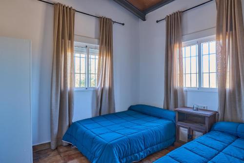 1 Schlafzimmer mit 2 blauen Betten und 2 Fenstern in der Unterkunft Casa Rural Olivar de la Marquesa in La Carlota