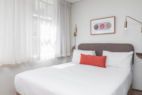 a bedroom with a white bed with a red pillow at Habitat Aparthotel by Totalstay in Cape Town