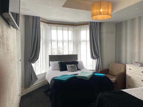 a bedroom with a bed and a chair and windows at Villa Guest House in Porthcawl