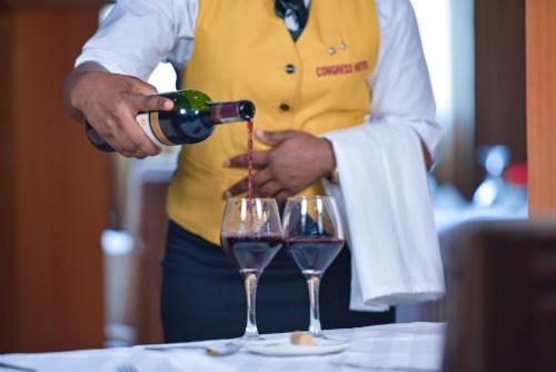 a person pouring wine into two glasses on a table at CONGRESS HOTEL Yaoundé in Yaoundé