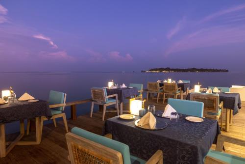 a restaurant with tables and chairs with a view of the water at Angsana Velavaru In-Ocean Villas in Dhaalu Atoll