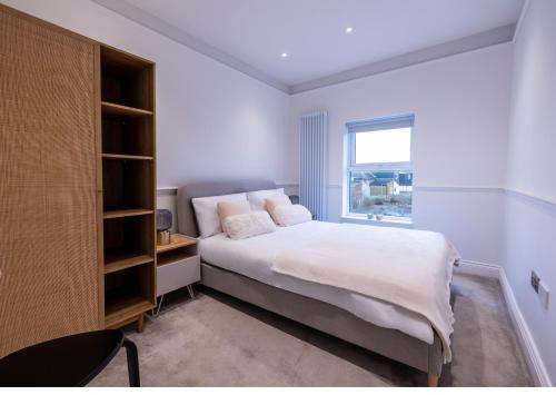 a white bedroom with a bed and a window at The Stanley in Teddington
