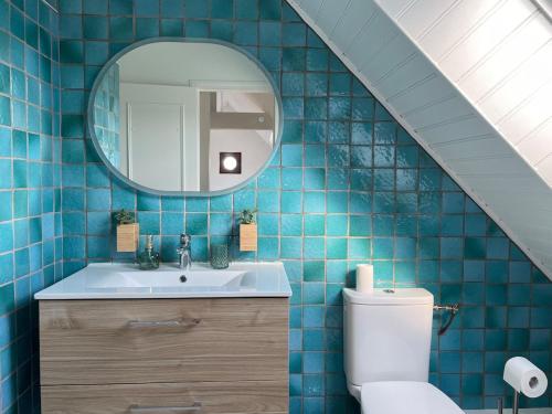 La salle de bains est pourvue de carrelage bleu, d'un lavabo et d'un miroir. dans l'établissement Domaine de Kernizan, à Plouharnel