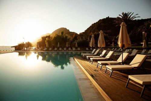 a group of chairs and umbrellas next to a swimming pool at Domes of Corfu, Autograph Collection in Glyfada