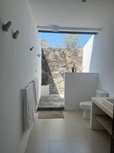 a bathroom with a toilet and a stone wall at ekasboardriders surf&stay in Ekas
