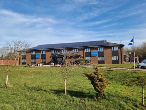a building with a grass field in front of it at Travel Plaza Hotel in Desborough
