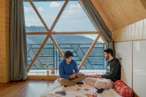 two men sitting on a bed in a room with a window at The Bagh Kufri in Kūfrī