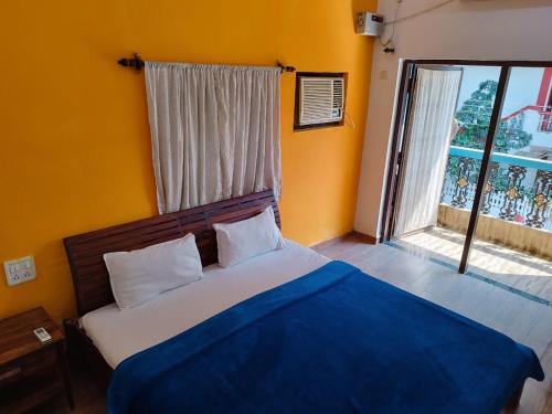 a bedroom with a bed with a blue blanket and a window at Calangute Rocks Inn in Calangute