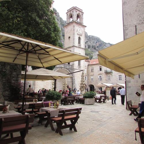 a patio with tables and umbrellas with a clock tower at Apartments Popovic in Kotor
