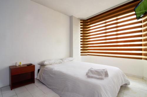 a bedroom with a white bed and a wooden window at Deportel Bogotá in Bogotá