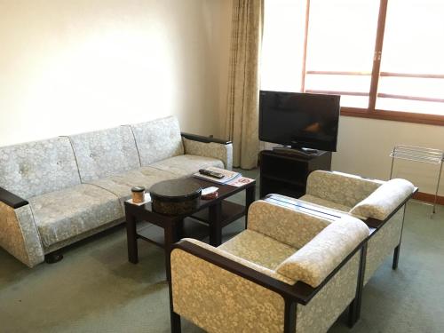a living room with a couch and chairs and a tv at Nikko Astraea Hotel in Nikko