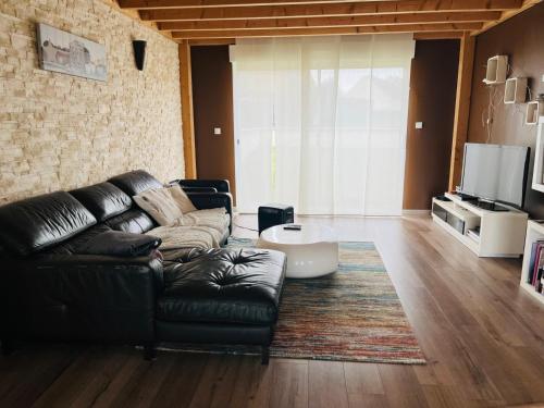 a living room with a black leather couch and a tv at Maison proche Circuit des 24h du Mans in Saint-Gervais en-Belin