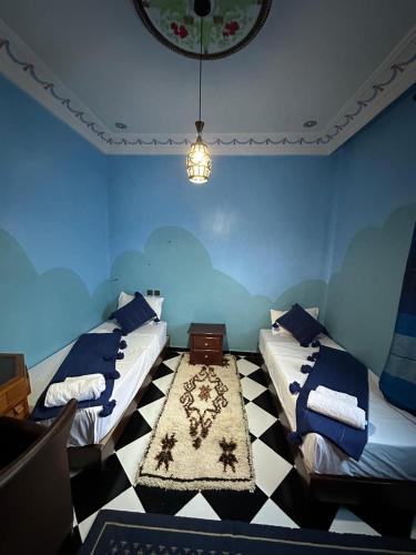 two beds in a blue room with a checkered floor at Riad Dar Fadma in Ouarzazate