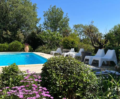 - une piscine avec des chaises blanches et des fleurs violettes dans l'établissement La Sokina, à Grimaud